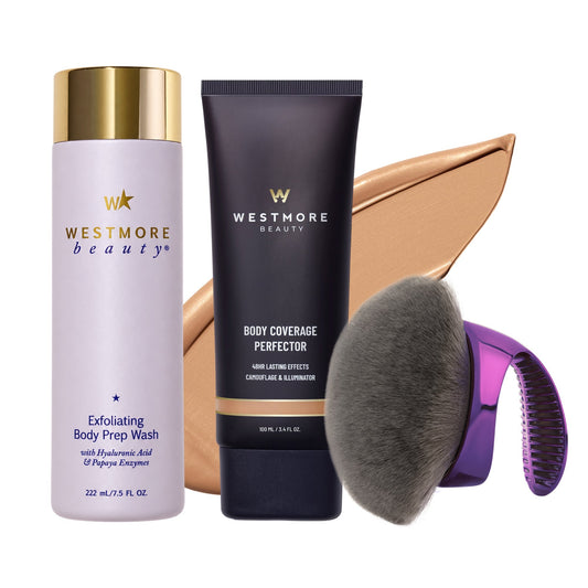 Westmore Beauty hair care set featuring Exfoliating Body Prep Wash in a lavender bottle with a gold cap, Body Coverage Perfector in a dark navy tube with a gold band, a large makeup brush, and a purple-to-pink gradient hair comb, arranged against a white background with a beige makeup smear behind them.