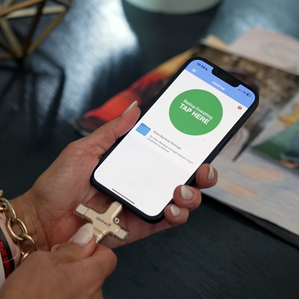 Person holding a smartphone with a backup app screen, wearing a gold bracelet.