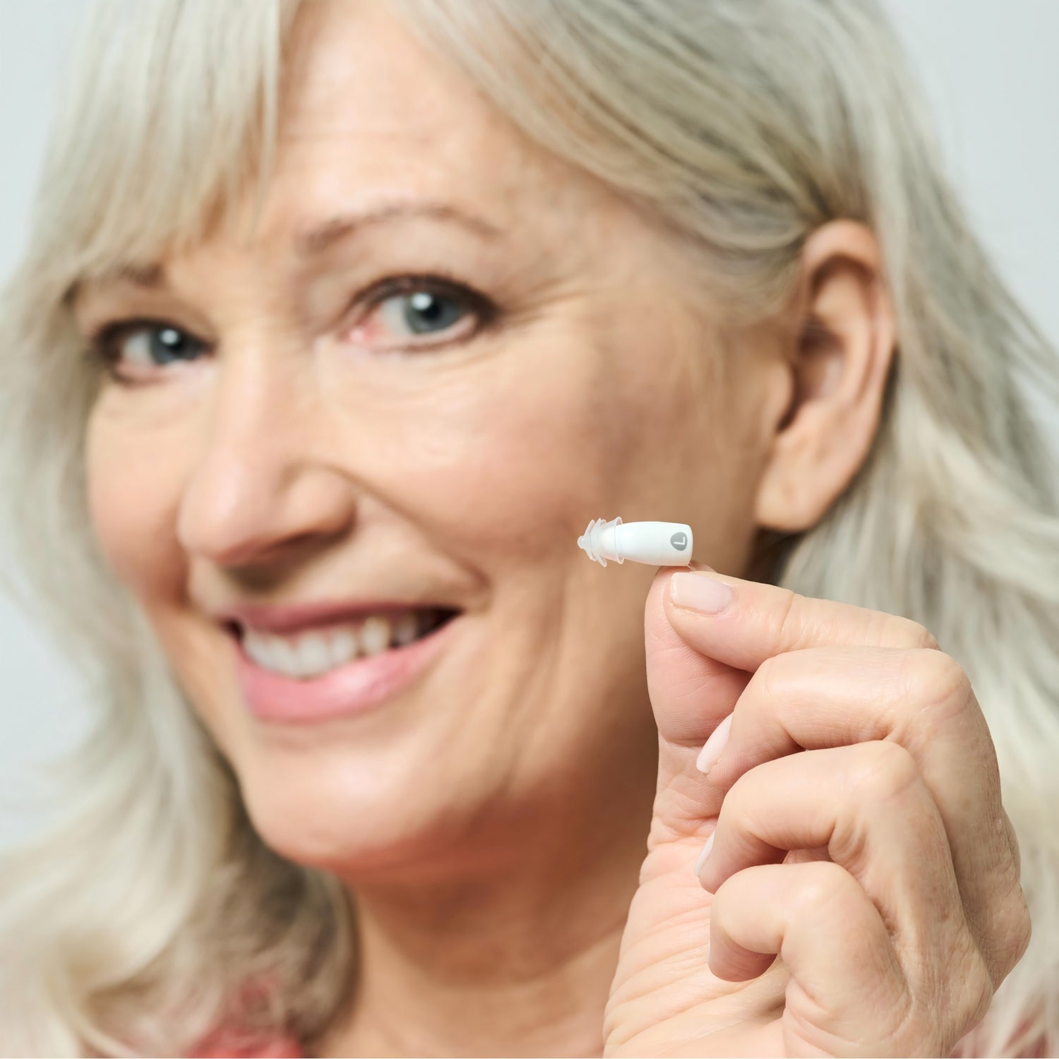Woman holding a small white device near her ear against a light background