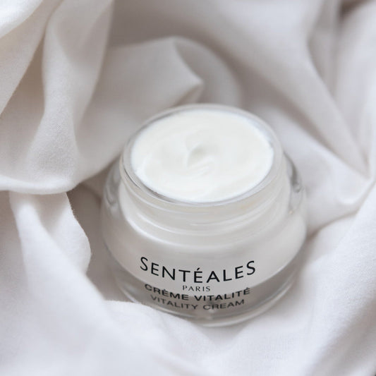 Jar of Senteaèles Paris Crème Vitalité on a woven mat with a pink flower in the background.
