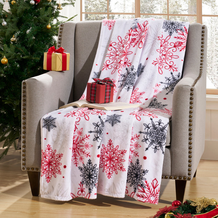 Decorative blanket with snowflake pattern draped over a chair next to a Christmas tree and presents.
