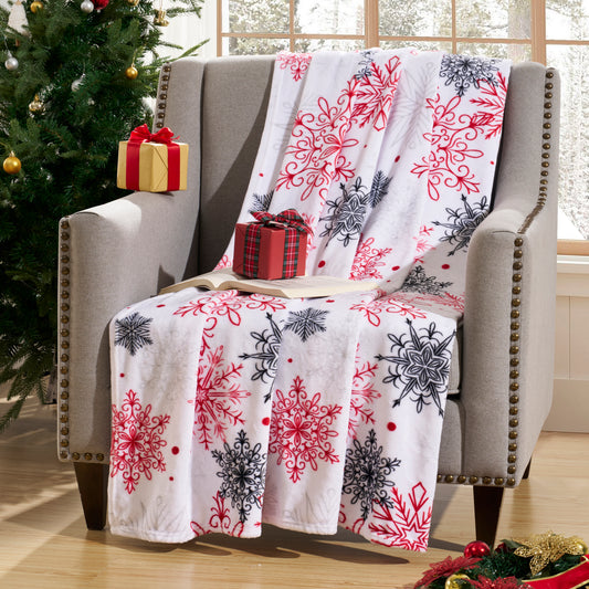Decorative blanket with snowflake pattern draped over a chair next to a Christmas tree and presents.