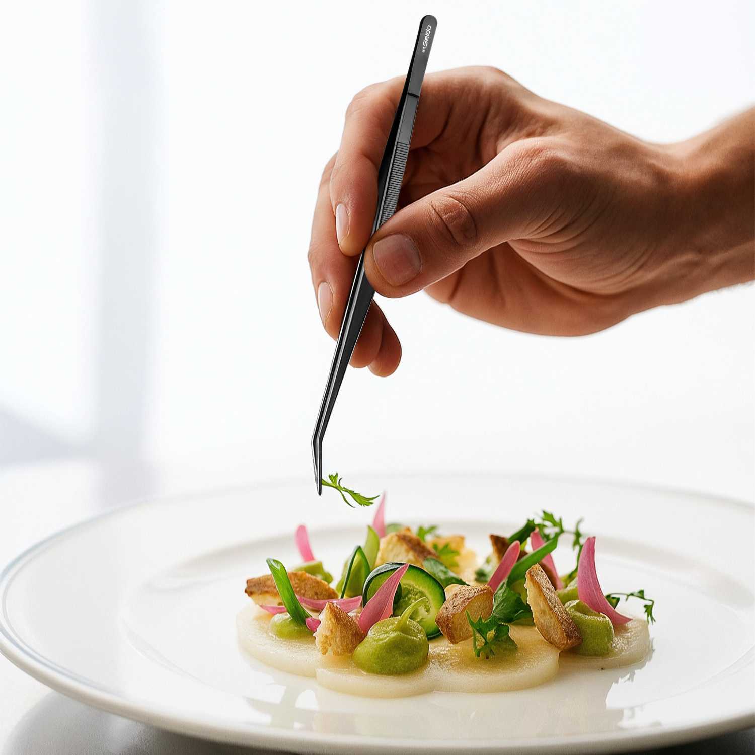 Hand using tweezers to place a garnish on a dish of food