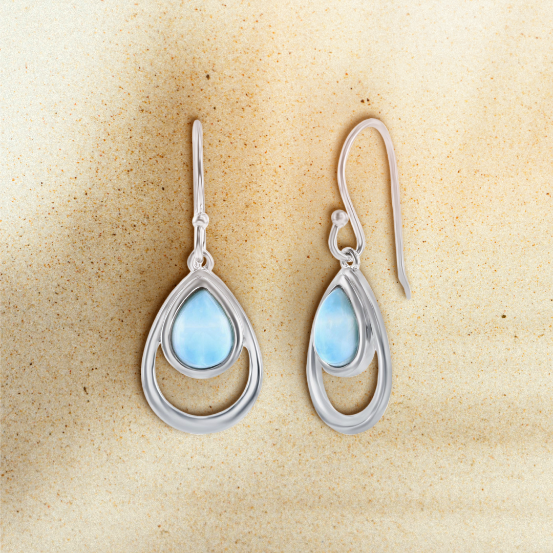 Silver teardrop earrings with blue gemstones on a beige background