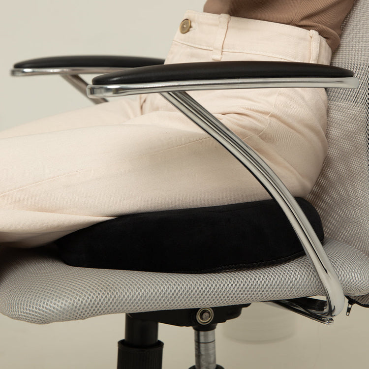 Person sitting on a chair with armrests and a beige cushioned seat.