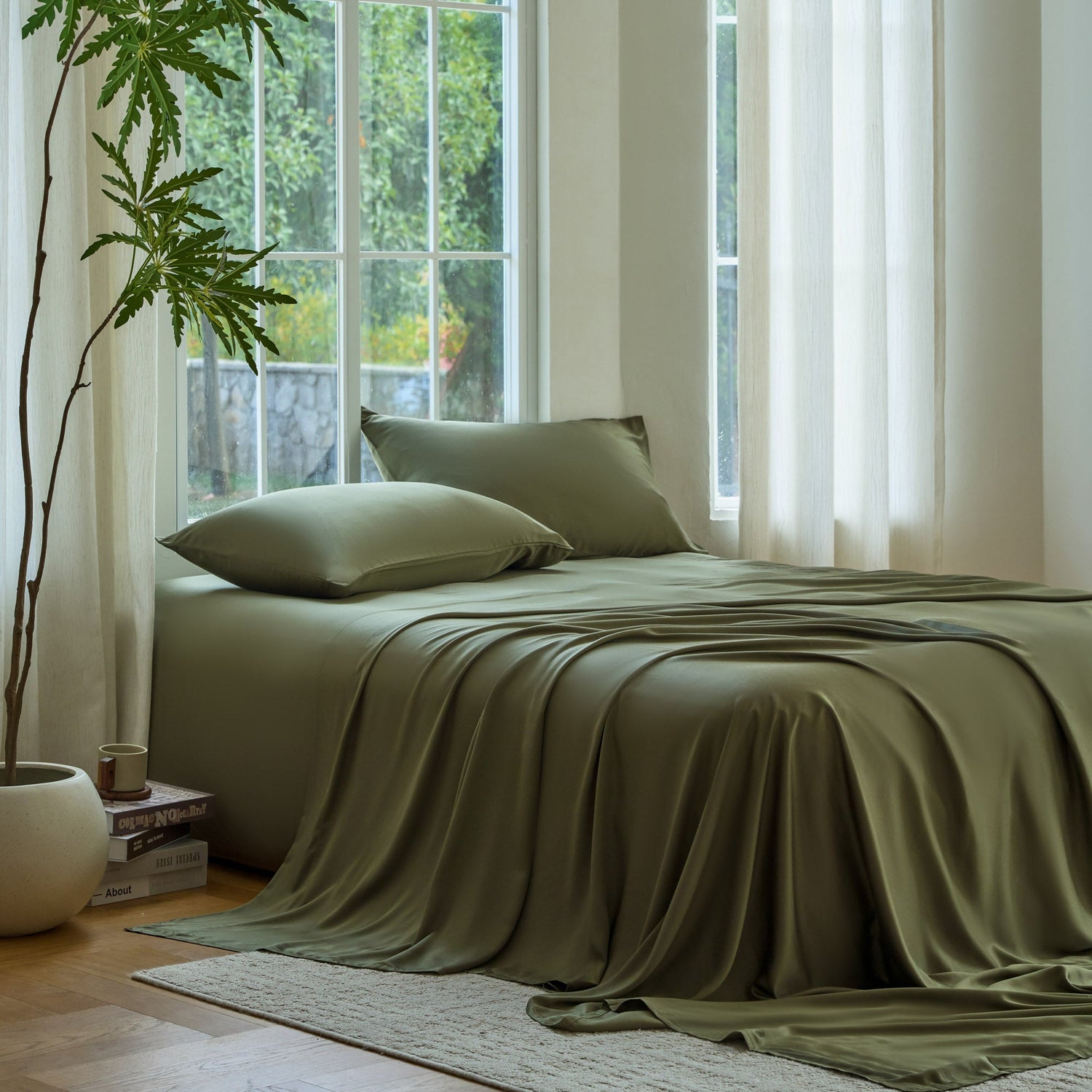 Bed with green bedding in a bright room with large windows and a plant.