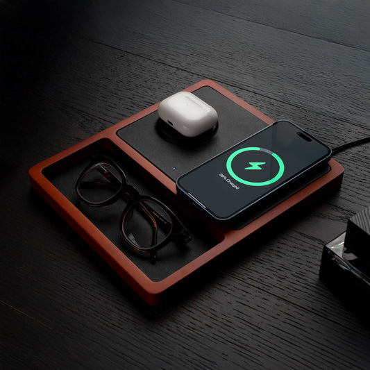 A black and oak wood 2-in-1 MagSafe wireless charging pad with a smartphone and earbuds being charged on it.