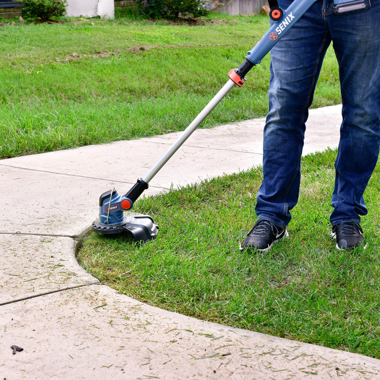 Person using a Senix string trimmer to cut grass along a sidewalk