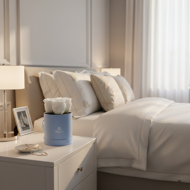 Neatly made bed with white bedding and pillows, nightstand with lamp and decorative items.