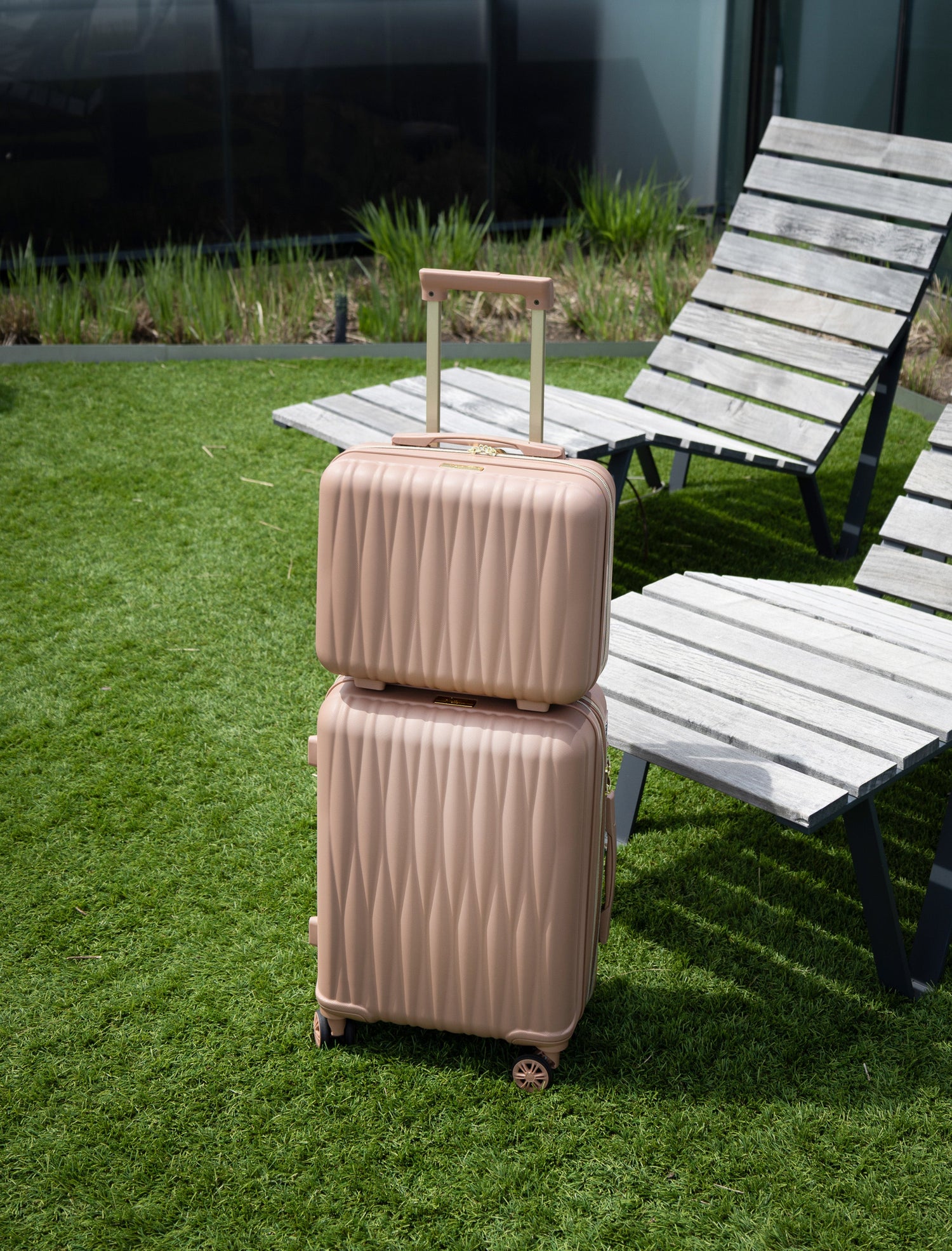 Two beige suitcases stacked on grass with a chair in the background