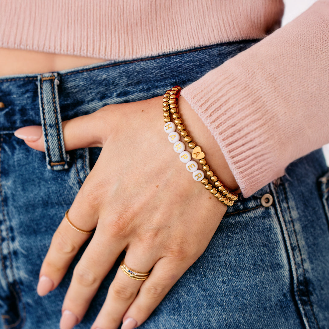 Hand wearing gold bracelets and rings on a denim background