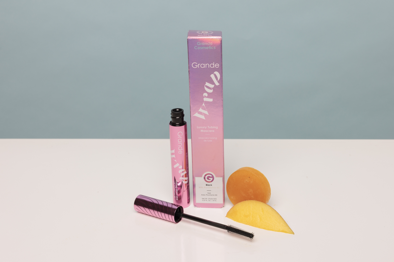 Cosmetic products including a pink tube, brush, and packaging on a white surface with a light blue background.