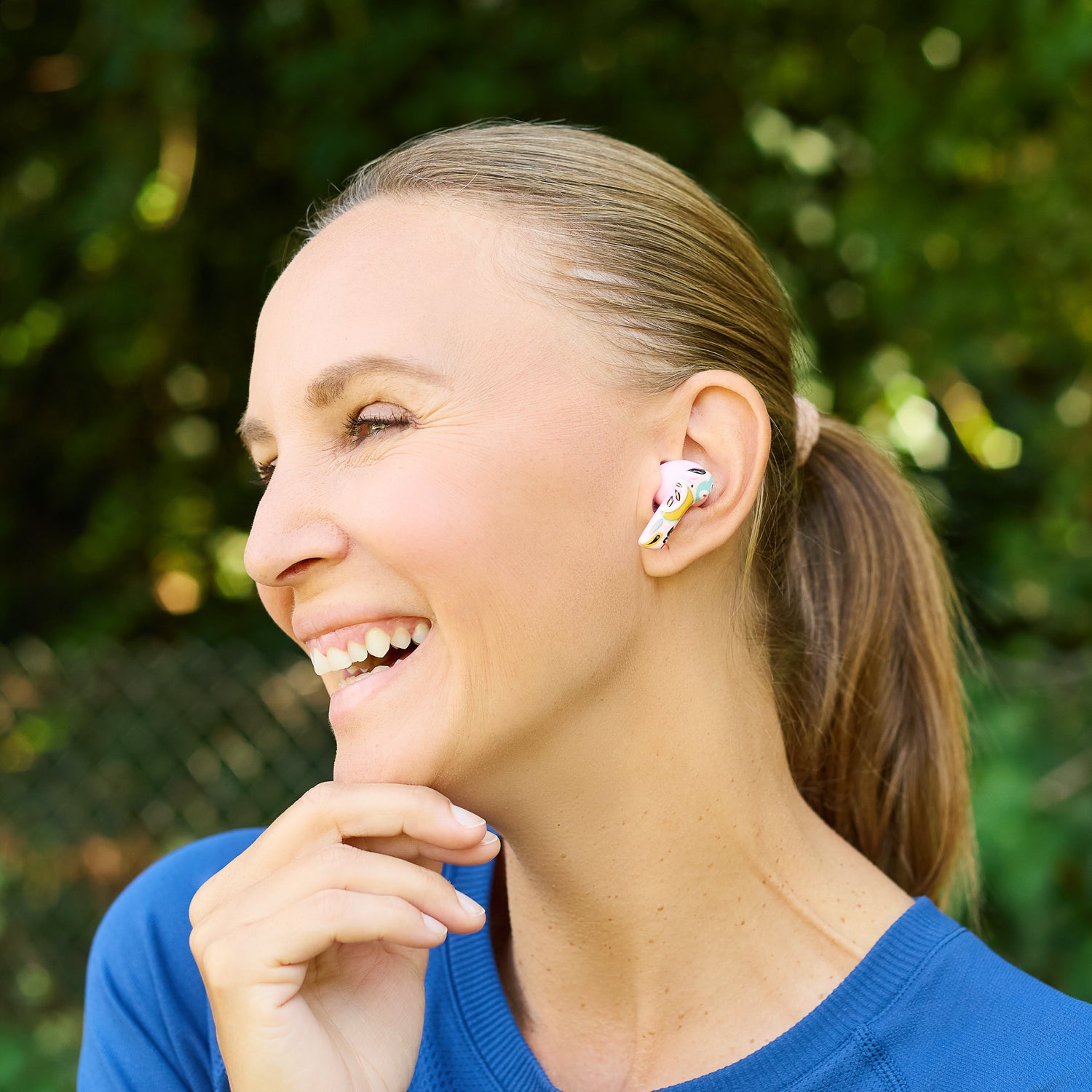 Woman wearing colorful earbuds outdoors with a blurred green background