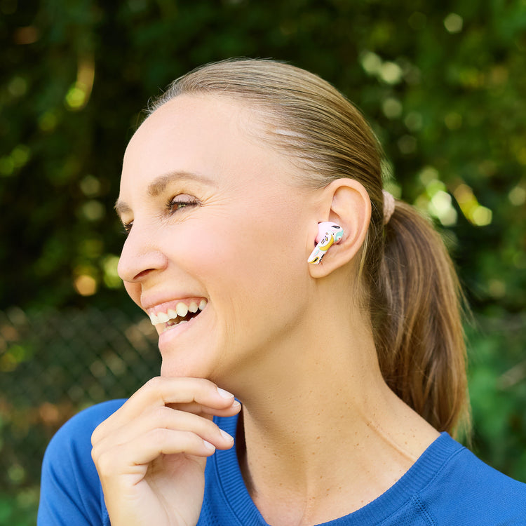 Woman wearing colorful earbuds outdoors with a blurred green background