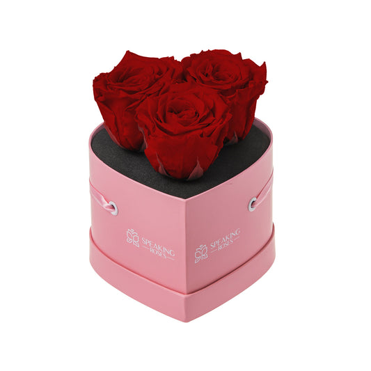 Pink heart-shaped box with three red roses on a white background