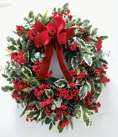 Christmas wreath with red berries, pine cones, and a red bow on a white background