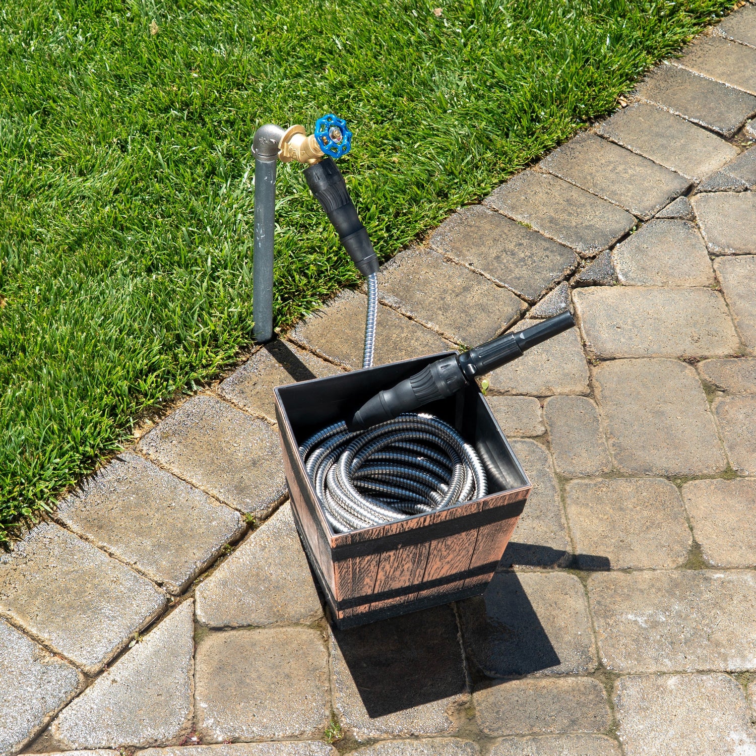 Outdoor garden hose with nozzle on a wooden stand on a stone patio.