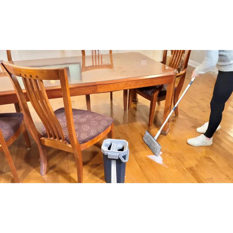 Person cleaning a wooden floor with a mop in a dining room setting