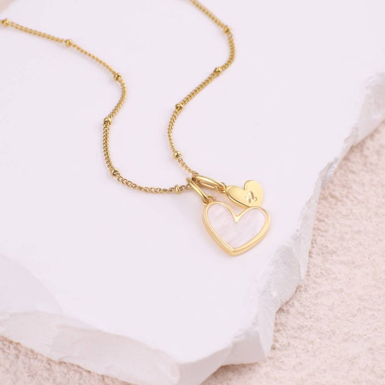 Gold necklace with a heart-shaped pendant on a white stone surface