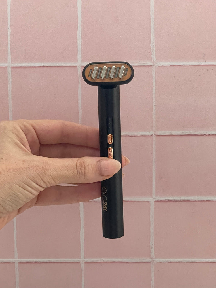 Hand holding a black electric razor against a pink tiled wall