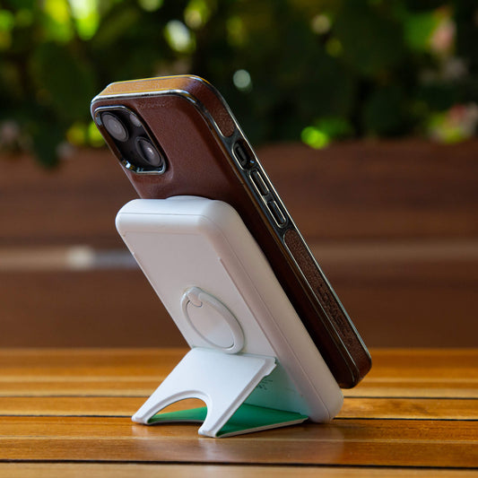 A white NYTSTND Pulse Power Bank with a green circle indicating the magnetic charging area, featuring an adjustable kickstand.