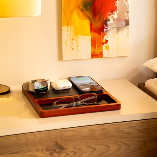 A wireless charging pad with integrated Apple Watch charger, featuring a black and oak design, with a smartphone, smartwatch, and earbuds being charged.