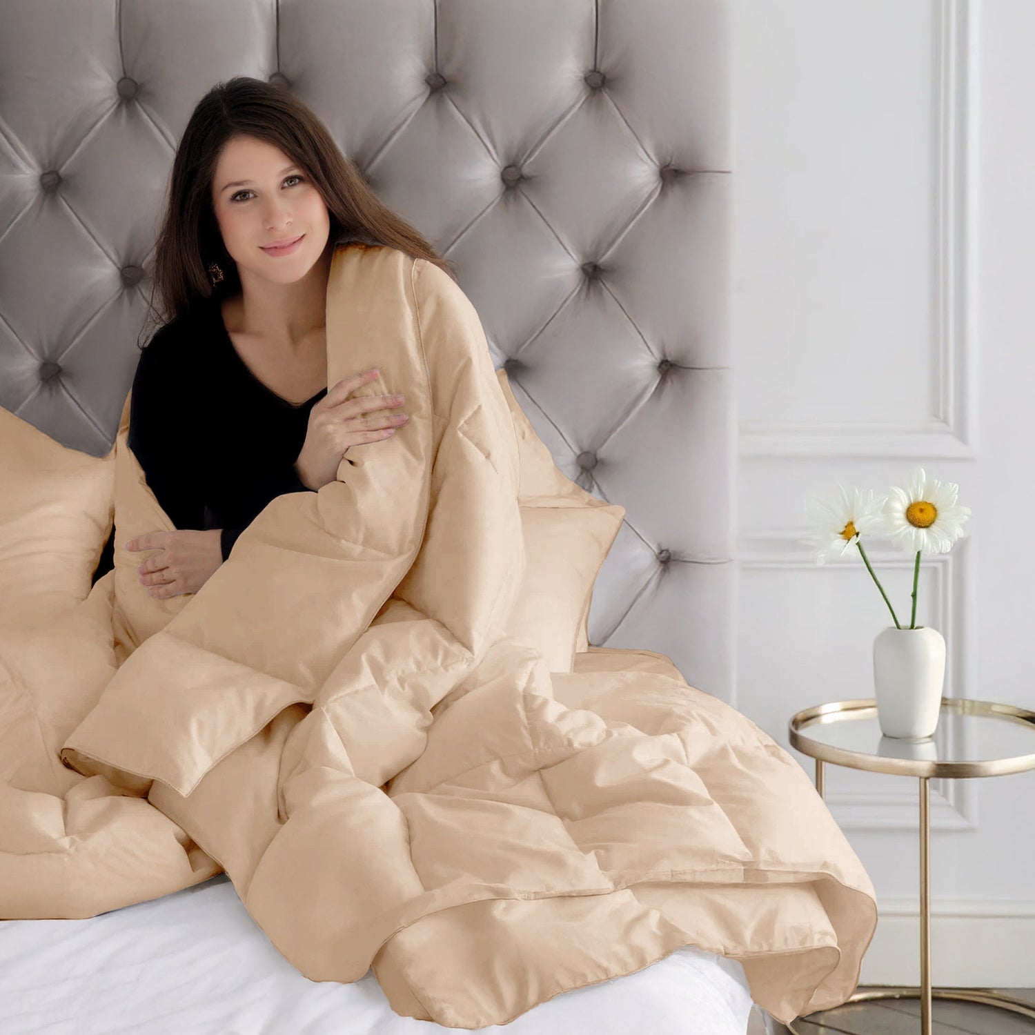 Woman wrapped in a beige blanket sitting on a bed with a tufted headboard.