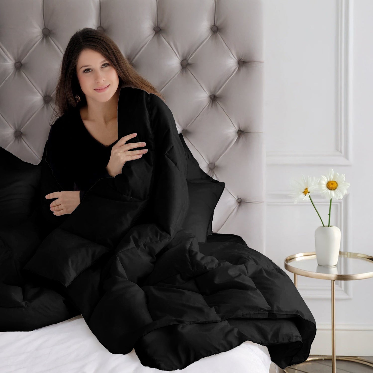 Woman wrapped in a black blanket sitting on a bed with a tufted headboard.