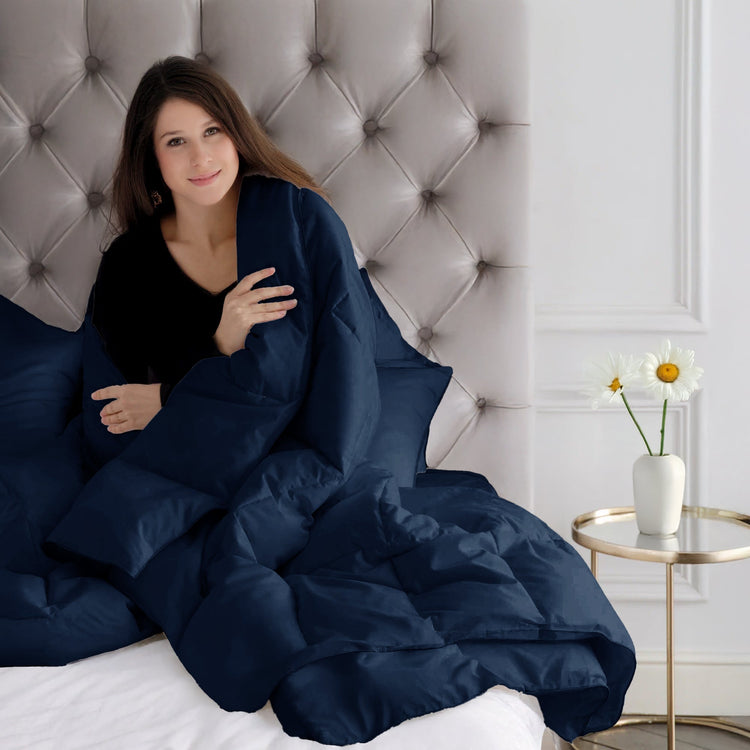 Woman wrapped in a navy blanket sitting on a bed with a tufted headboard.