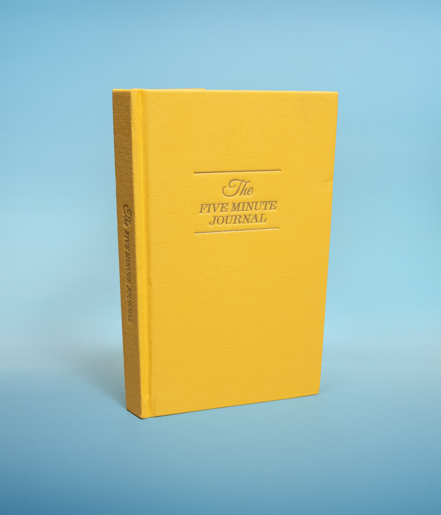 Yellow journal titled 'The Five Minute Journal' on a light blue background