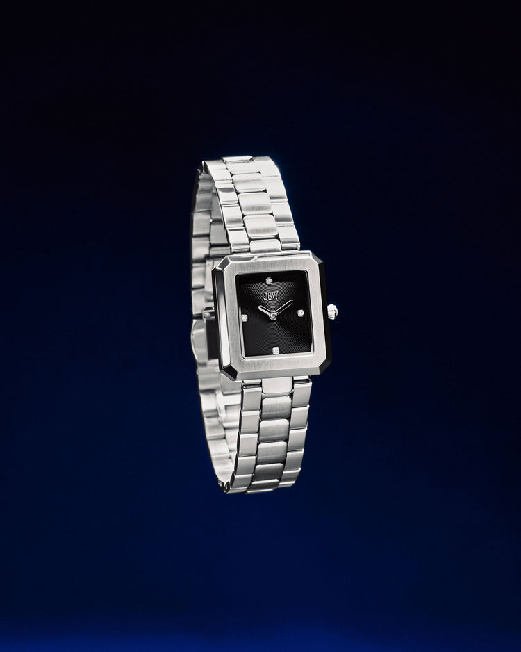 The JBW Watches Arc Single | J6390G is a gender-neutral silver wristwatch with a square black minimalist face, elegantly showcased on a dark blue gradient background.