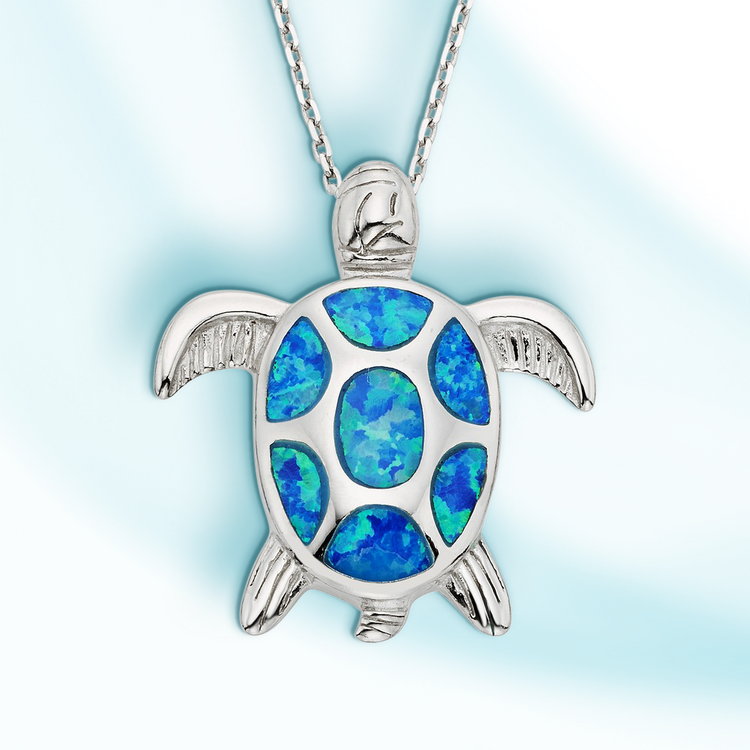 A sterling silver turtle pendant with blue inlay opal on a cable chain against a blue background.