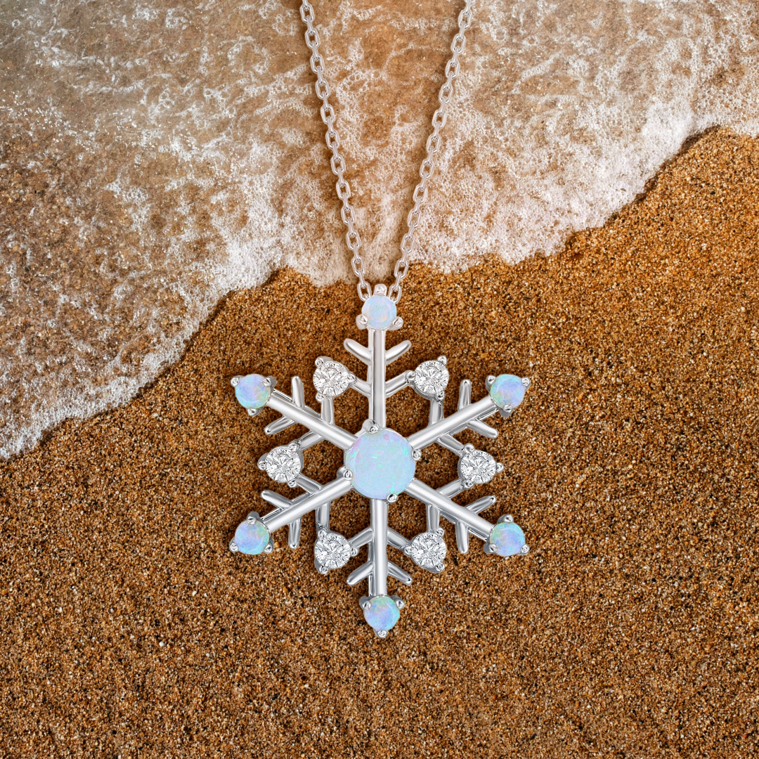 Snowflake-shaped necklace on sand with ocean waves
