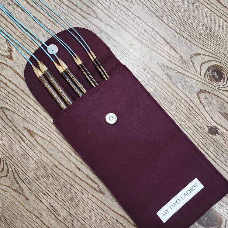Set of knitting needles in a purple case on a wooden surface
