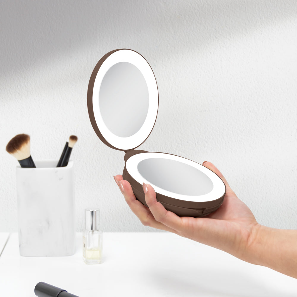 Hand holding a round, portable makeup mirror with LED lights on a neutral background