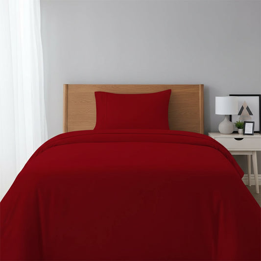 Red bedspread on a wooden bed with a white nightstand and decor items in the background.