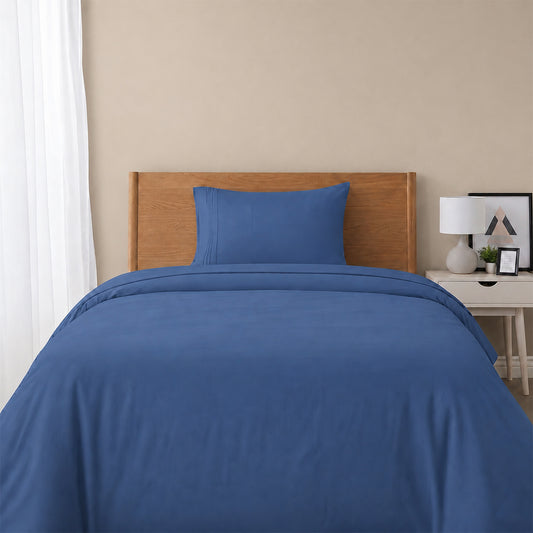 Red bedspread on a wooden bed with a white nightstand and decor items in the background.