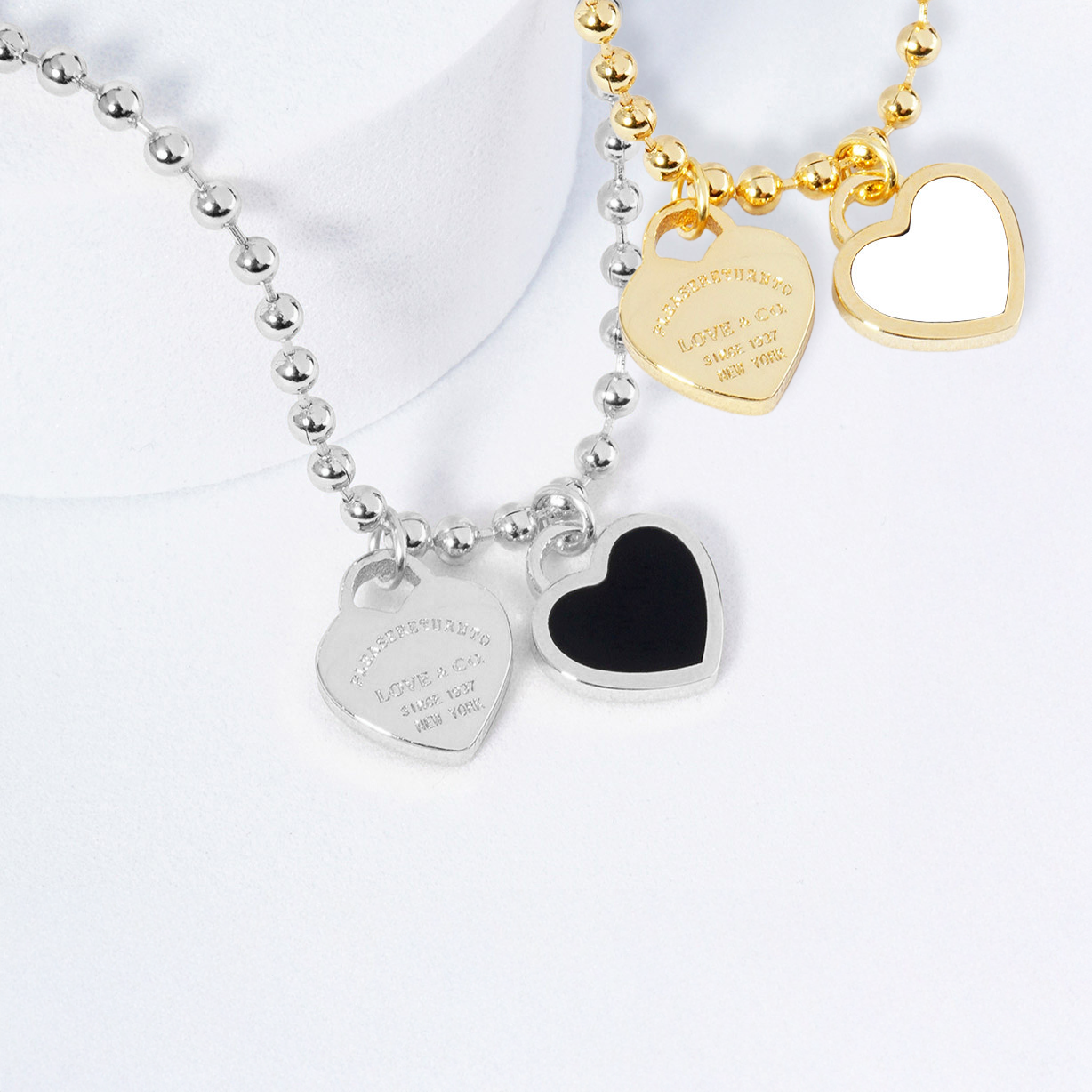 Two heart-shaped necklaces, one silver and one gold, on a white background.