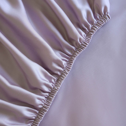 Bed with light purple bedding and pillows in a bright room with large windows.