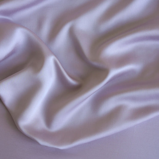 Bed with light purple bedding and pillows in a bright room with large windows.