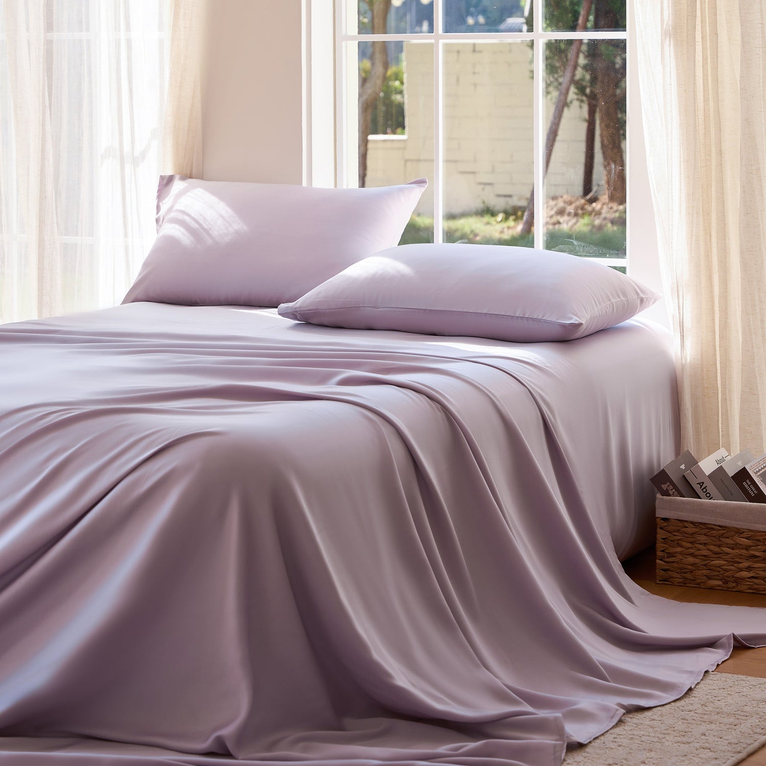 Bed with light purple bedding and pillows in a bright room with large windows.