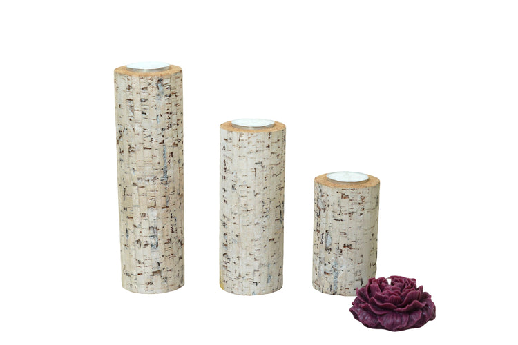 Three cylindrical candles with bark-like texture and a purple flower on a white background