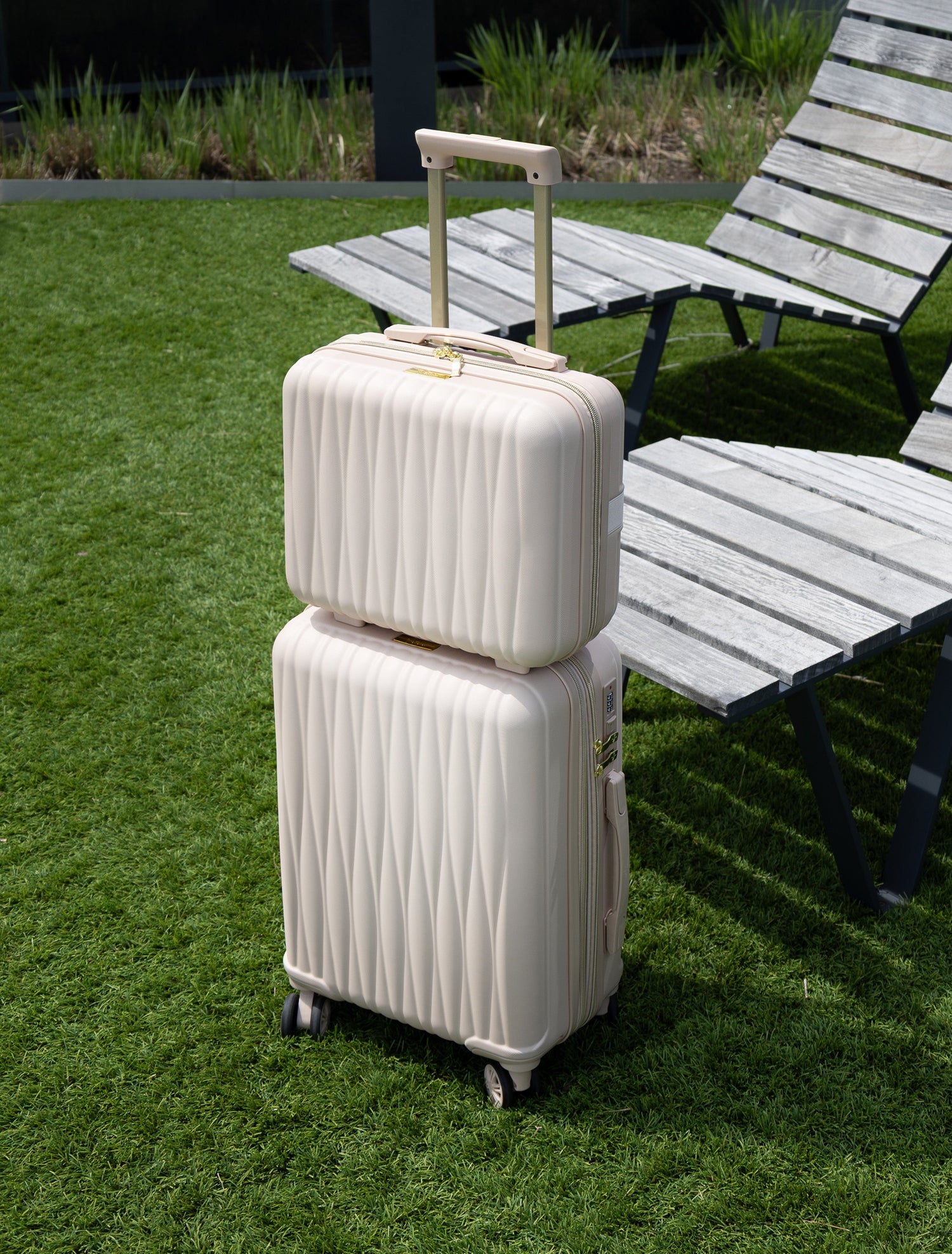 Two beige suitcases stacked on grass with lounge chairs in the background