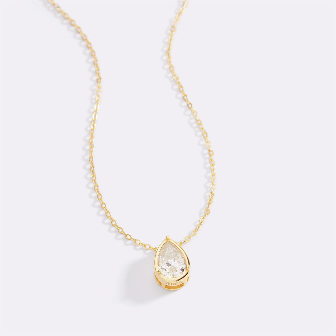 Gold necklace with a teardrop-shaped crystal pendant on a light gray background