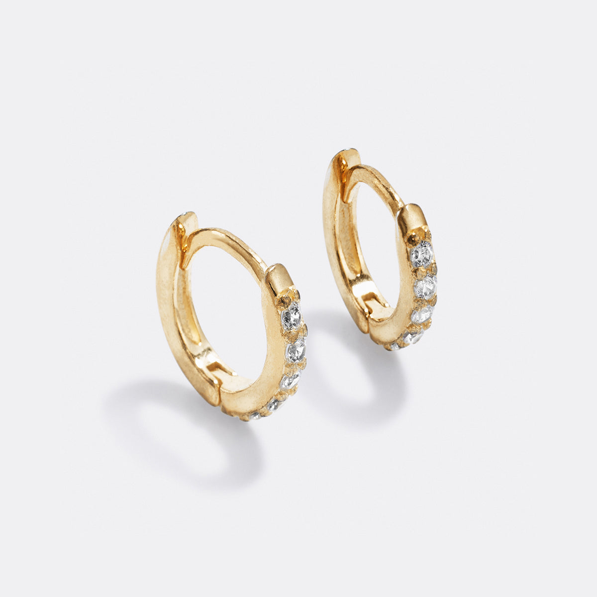 Gold hoop earrings with small diamonds on a light gray background