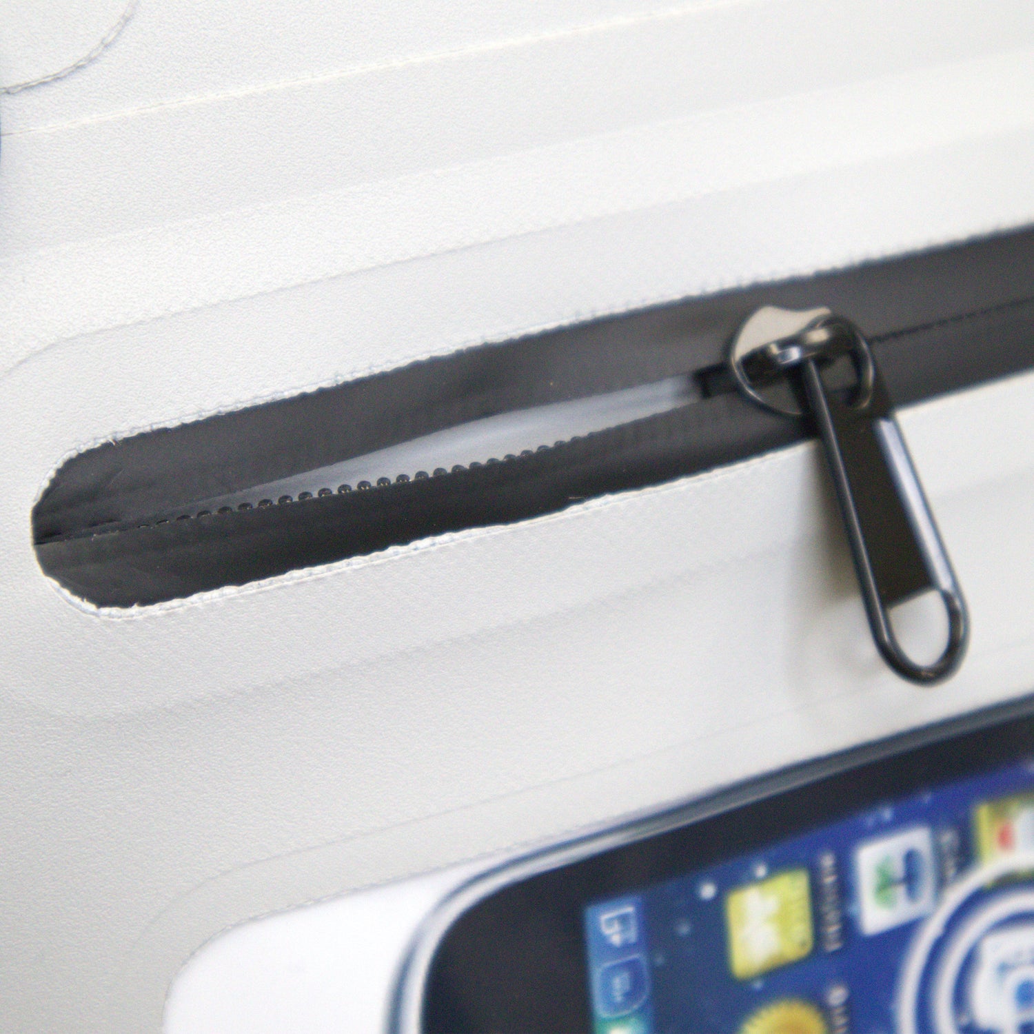 Close-up of a black zipper on a white surface with a smartphone partially visible.