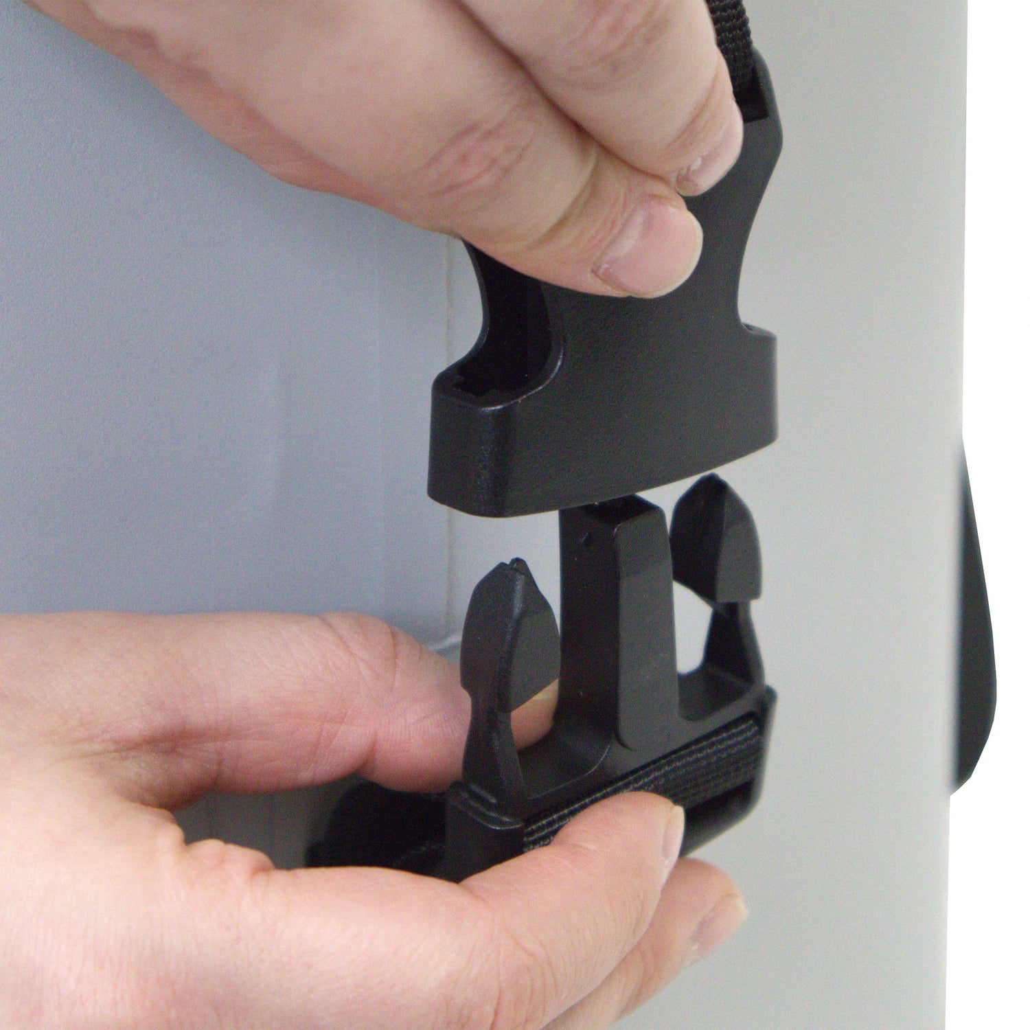 Black metal clip or holder being held by a person's hand against a gray background