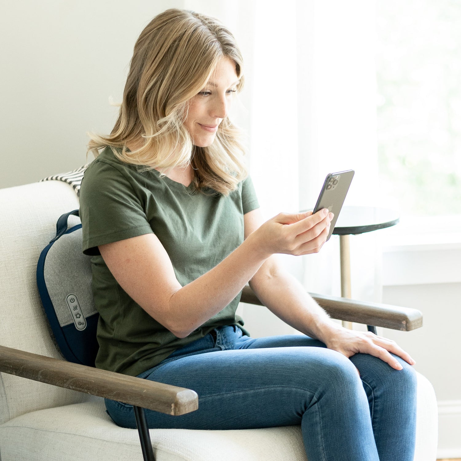 Woman sitting on a chair using a smartphone in a bright room.