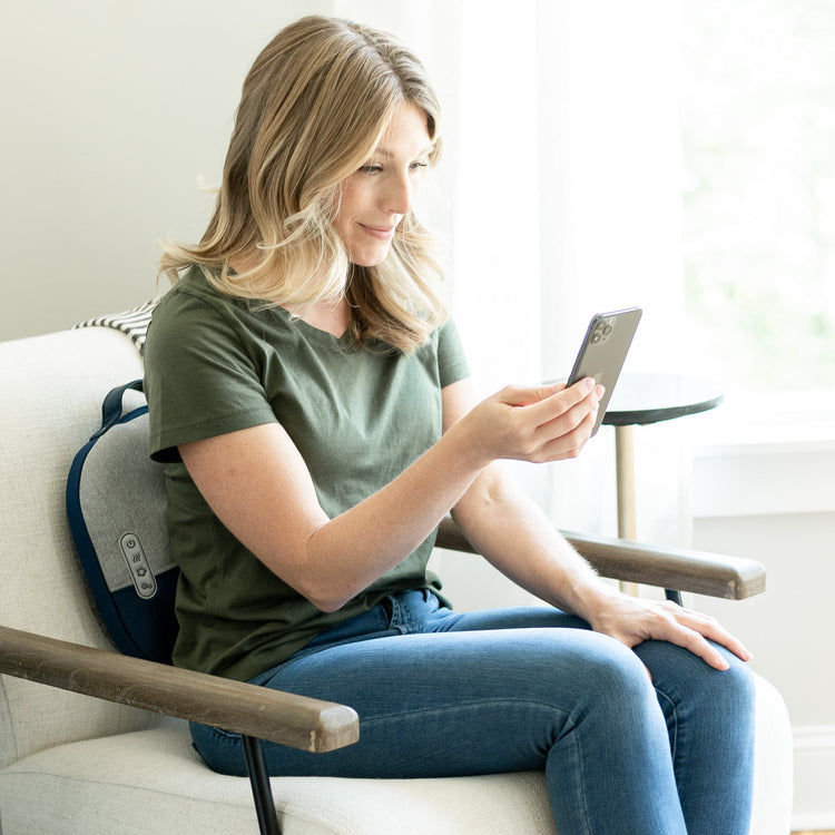 Woman sitting on a chair using a smartphone in a bright room.