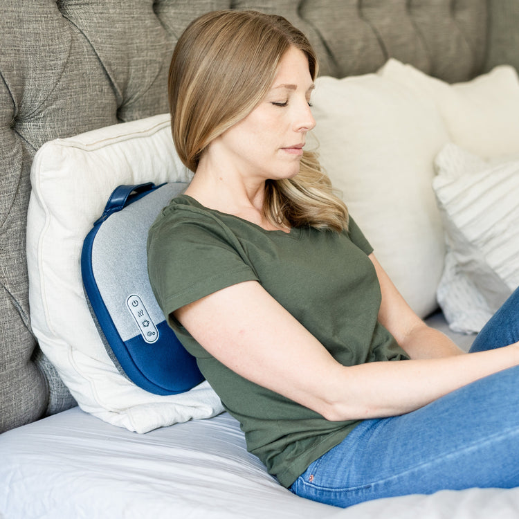 Woman using a back massager on a bed